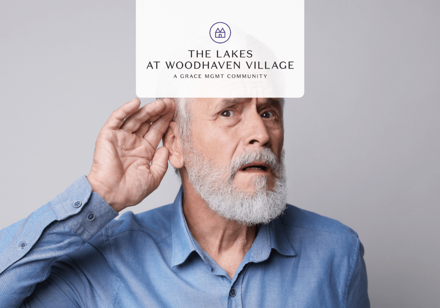 Older man with a gray beard listening intently, hand cupping his ear, wearing a blue shirt.